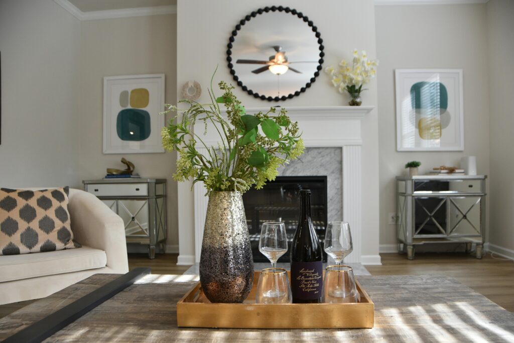 A modern living room featuring a decorative mirror, vase with flowers, and wine glasses on a wooden tray.
